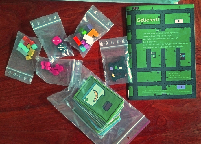 showing all game components: cards, trucks, parcels, houses, dice and manual
